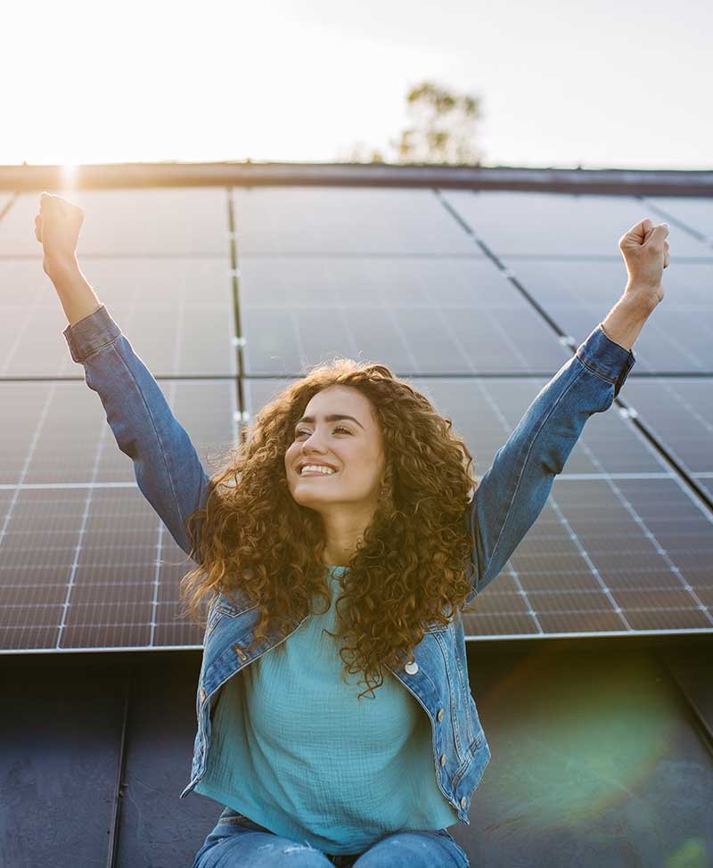 Woman smiling on a rooftop beside newly installed solar panels, celebrating clean renewable energy for her home in London.